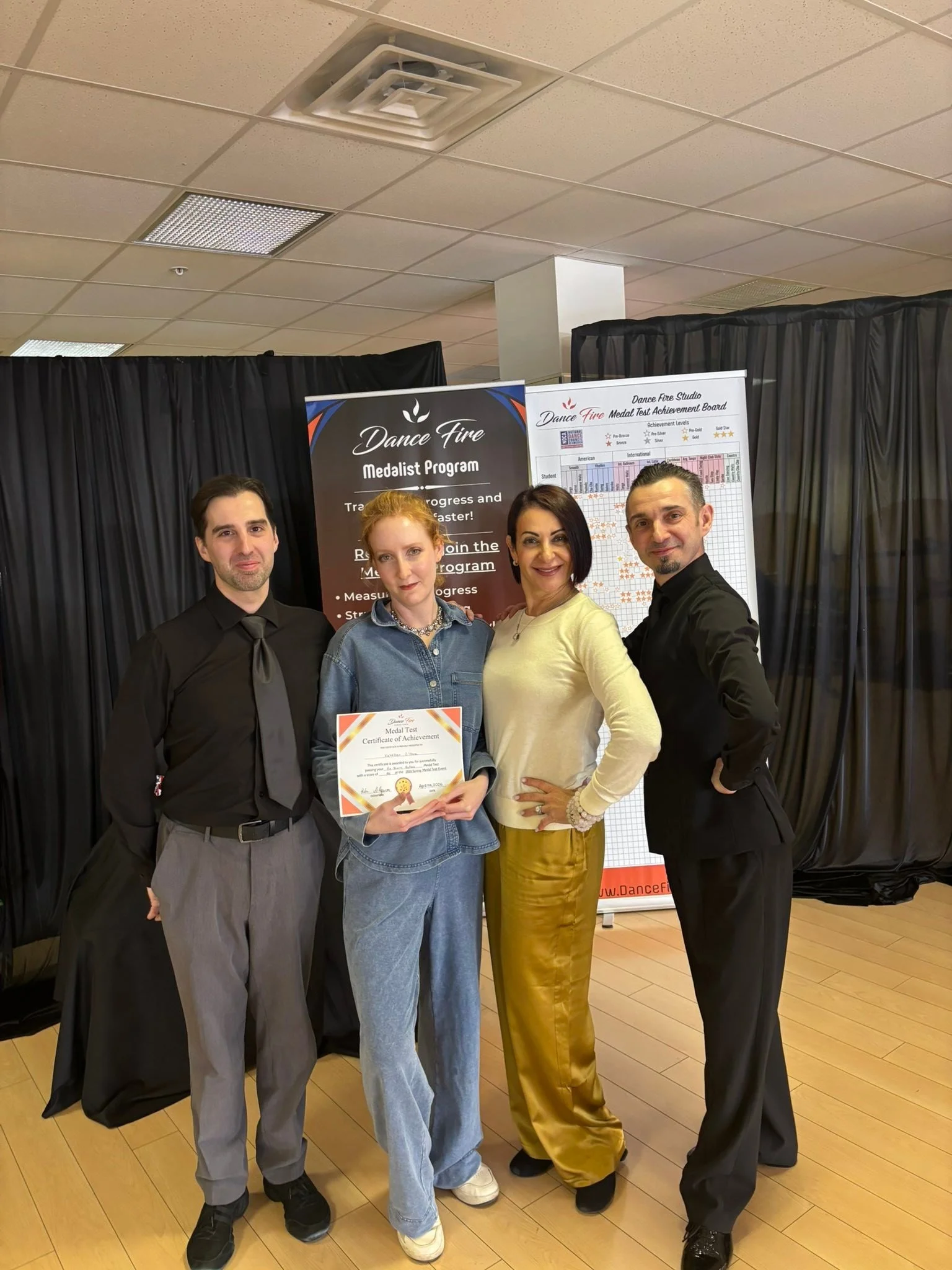 A participant in casual dance attire displays a spring achievement certificate