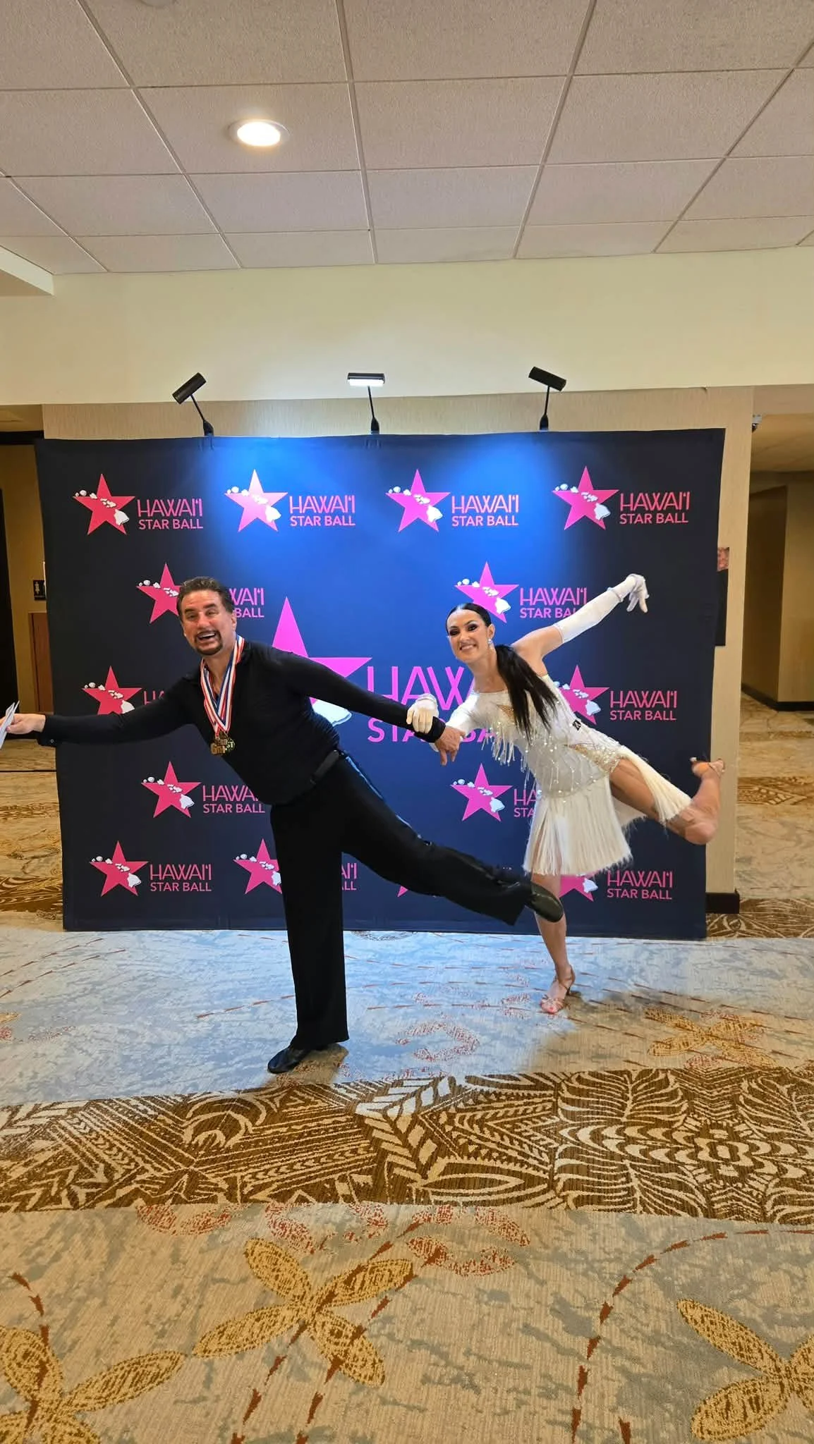A competition couple strikes a dance pose at the Hawaii Star Ball backdrop