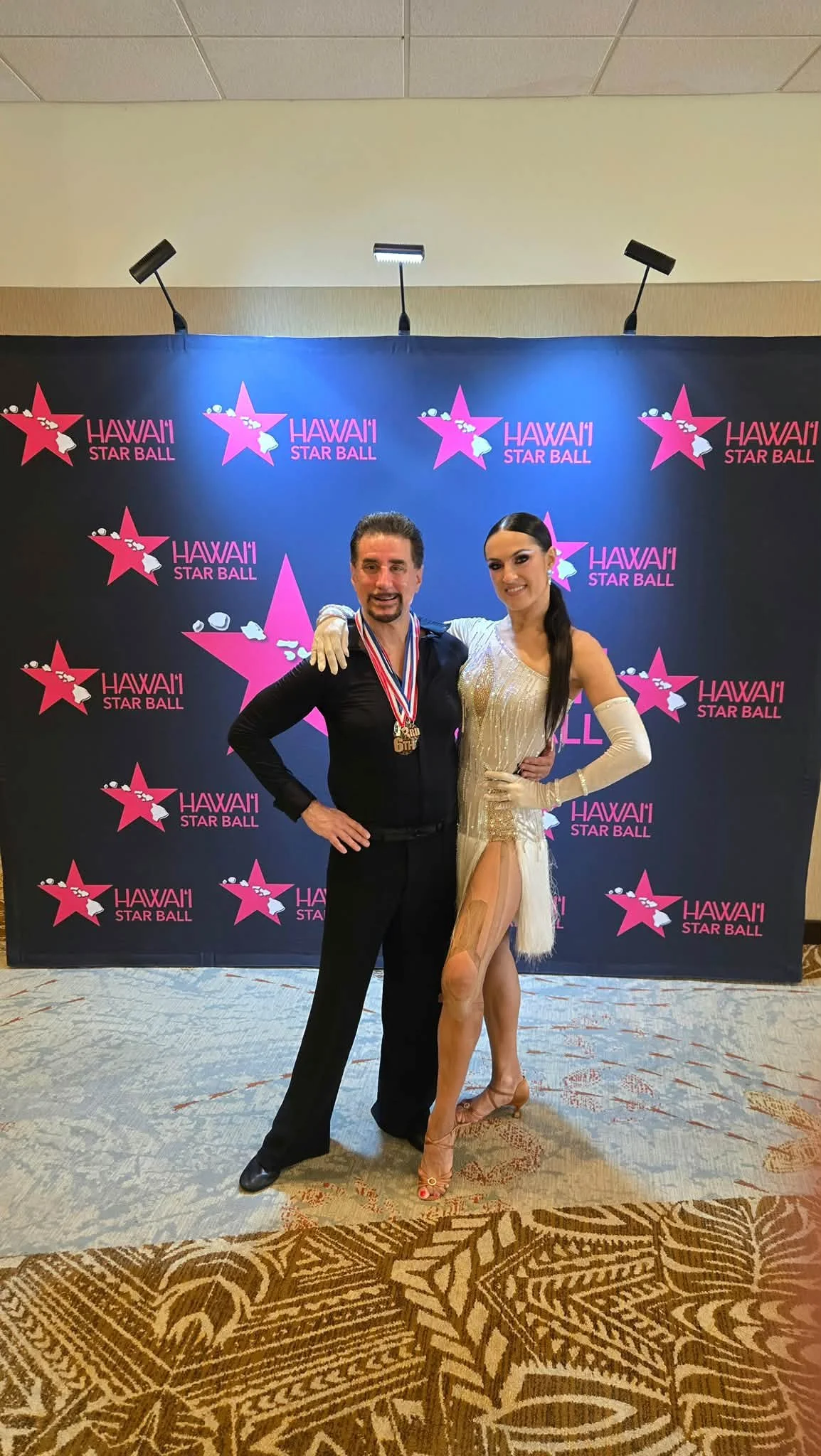 A Dance Fire pair poses with medals at the Hawaii Star Ball photo backdrop