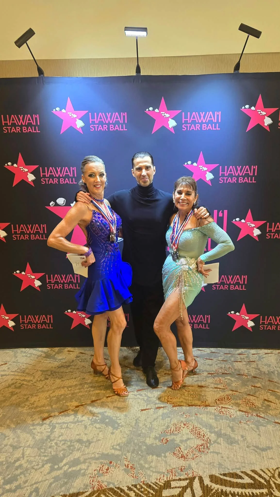 Dance Fire competitors pose with medals at the Hawaii Star Ball backdrop