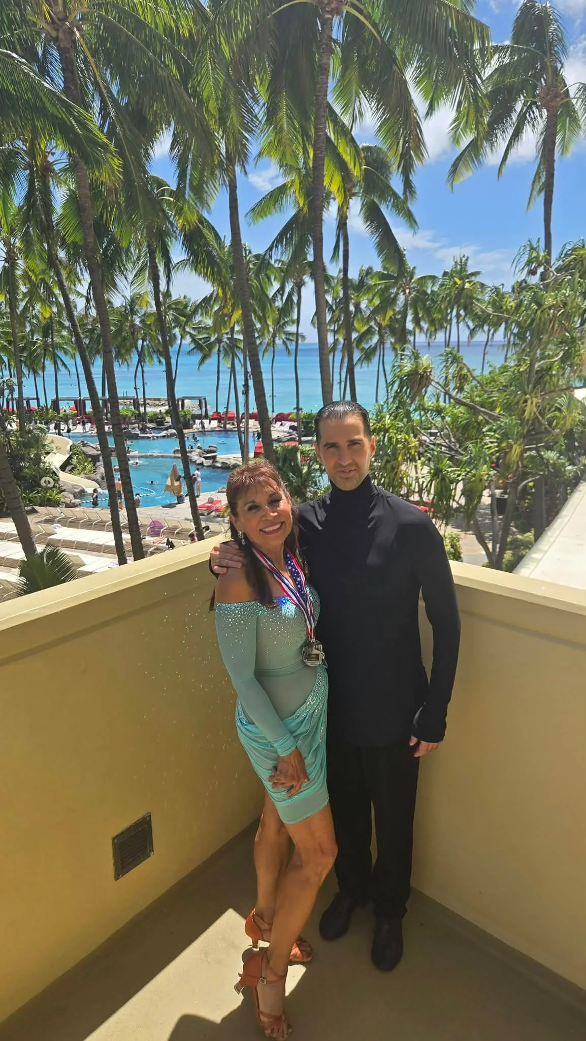 A competition pair poses on a palm-lined balcony in Hawaii