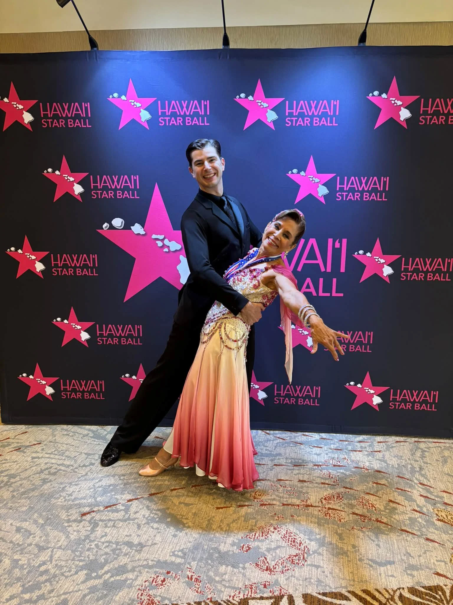 A ballroom couple holds a dramatic dip at the Hawaii Star Ball backdrop