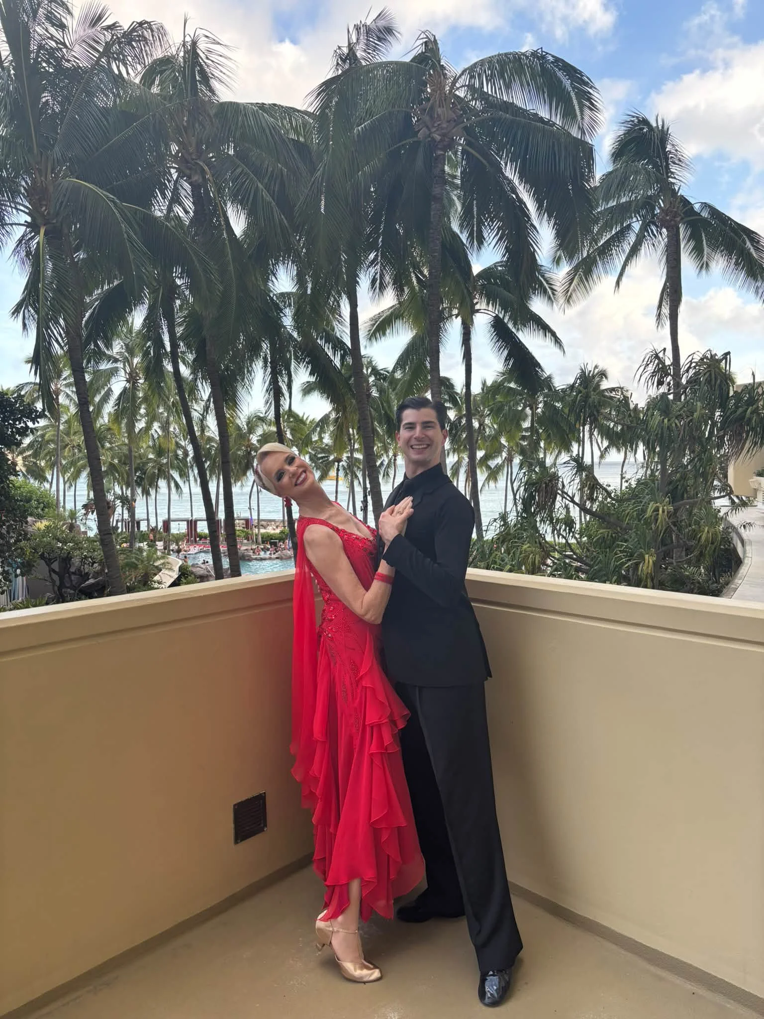 A competition pair poses on a Hawaii balcony in red and black attire