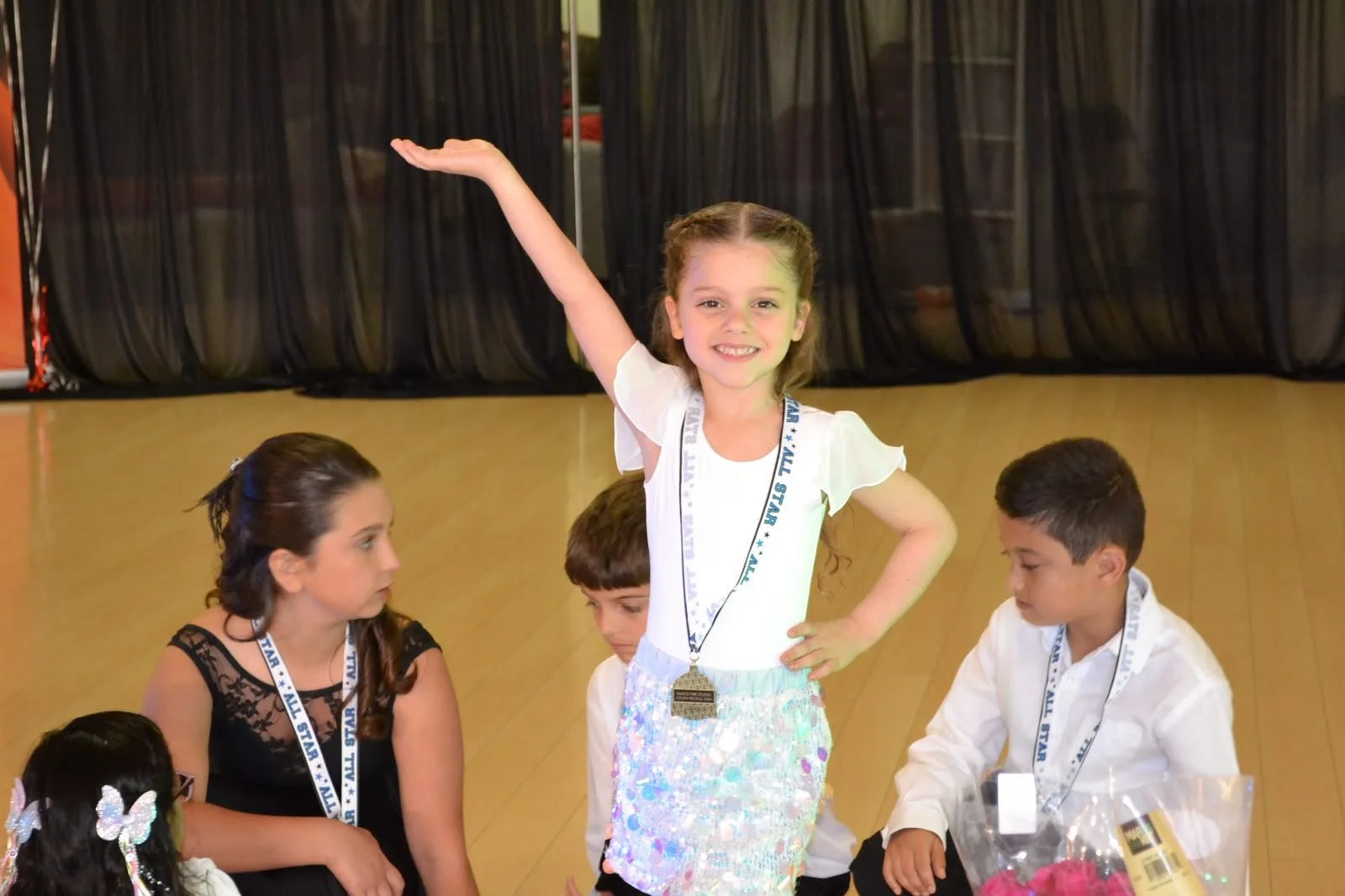 A young dancer wearing a medal strikes a celebratory pose