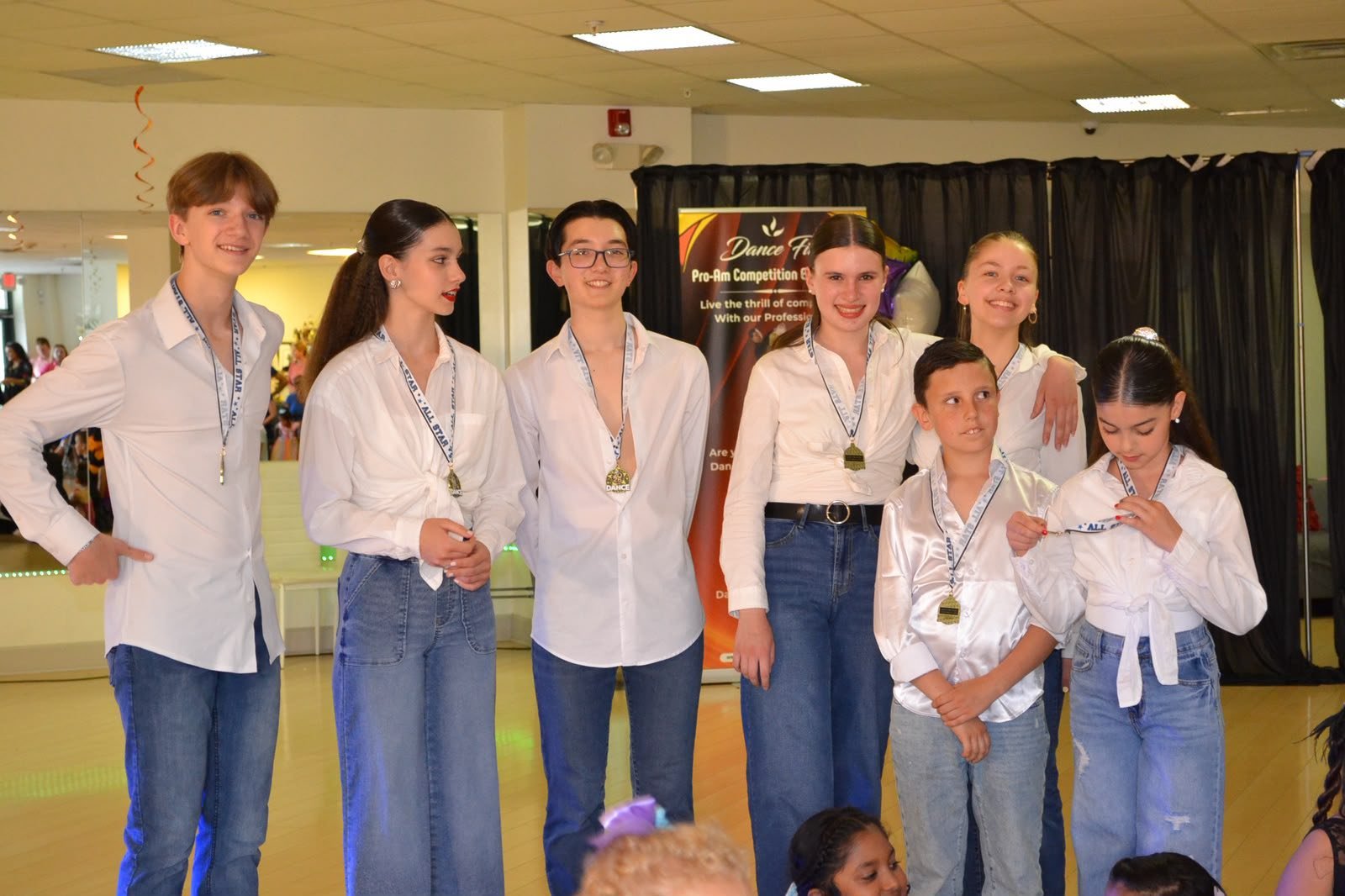 Young performers pose in white shirts and jeans after their recital routine