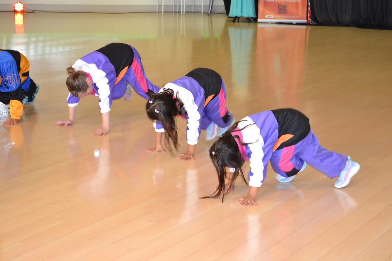 Children in purple costumes perform a coordinated floor movement