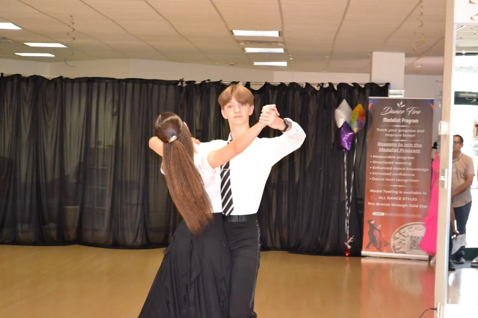 A young ballroom pair dances in hold before the recital backdrop