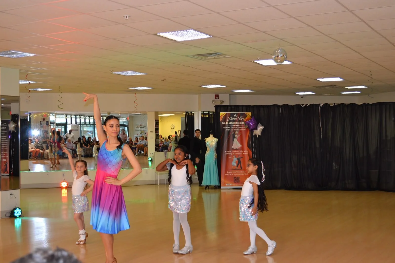Young dancers in colorful costumes perform across the studio floor