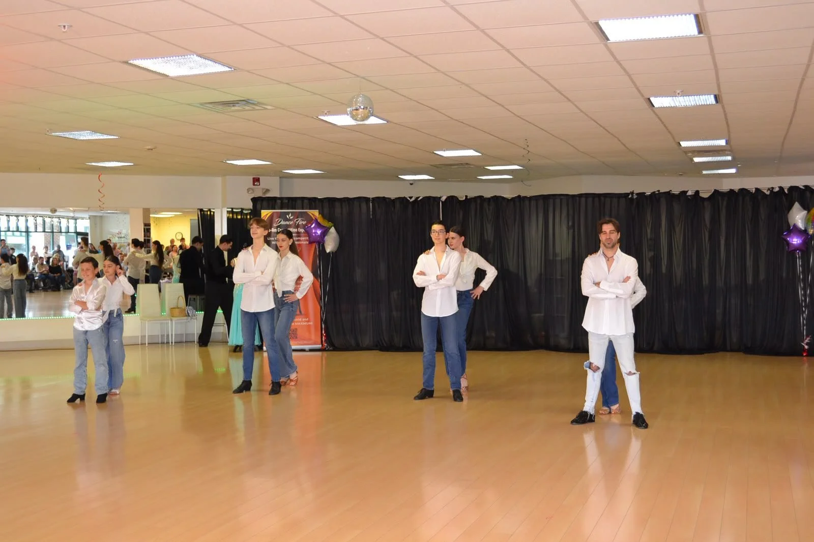 A group of young dancers in white shirts performs across the recital floor