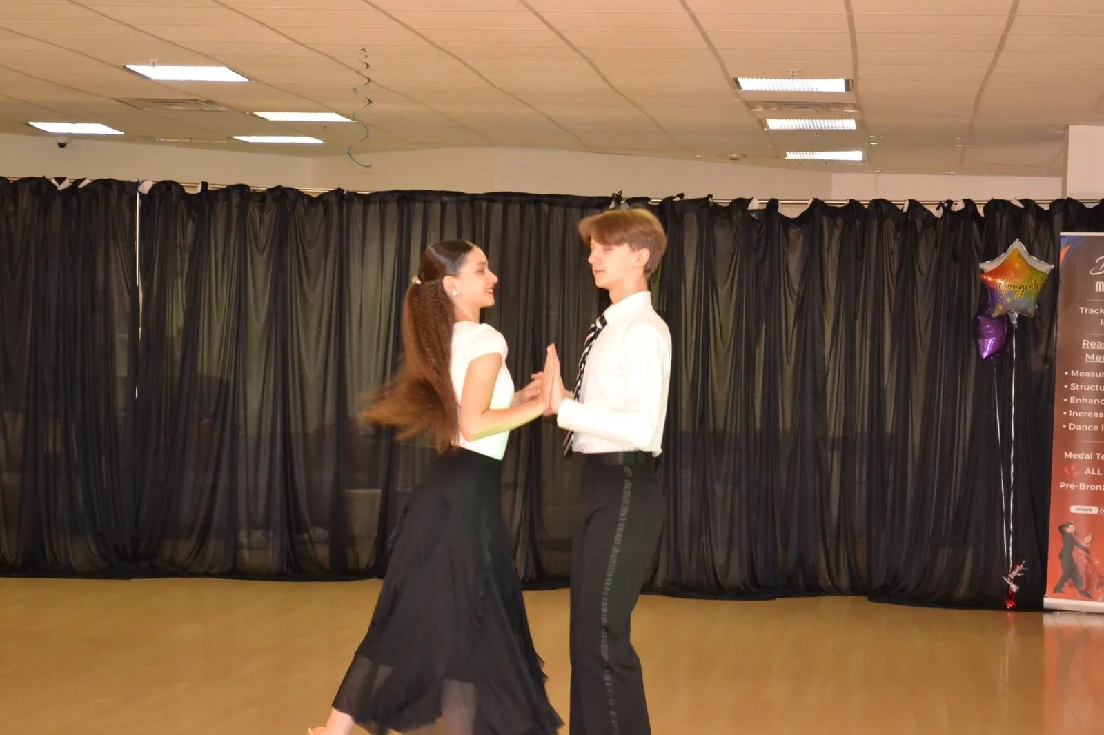 A youth ballroom pair dances together before the studio curtains