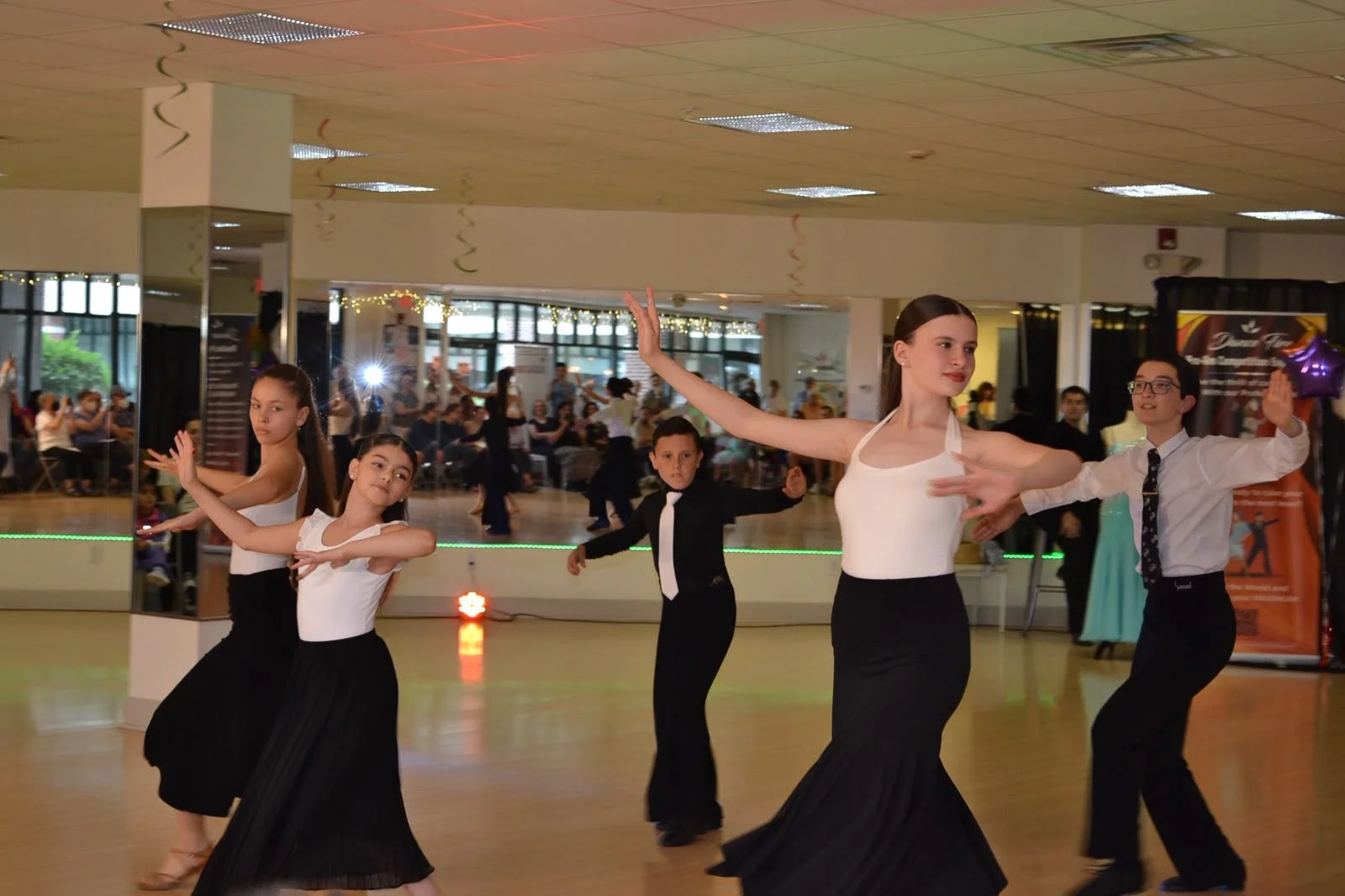 Young performers in white tops and black skirts extend their arms