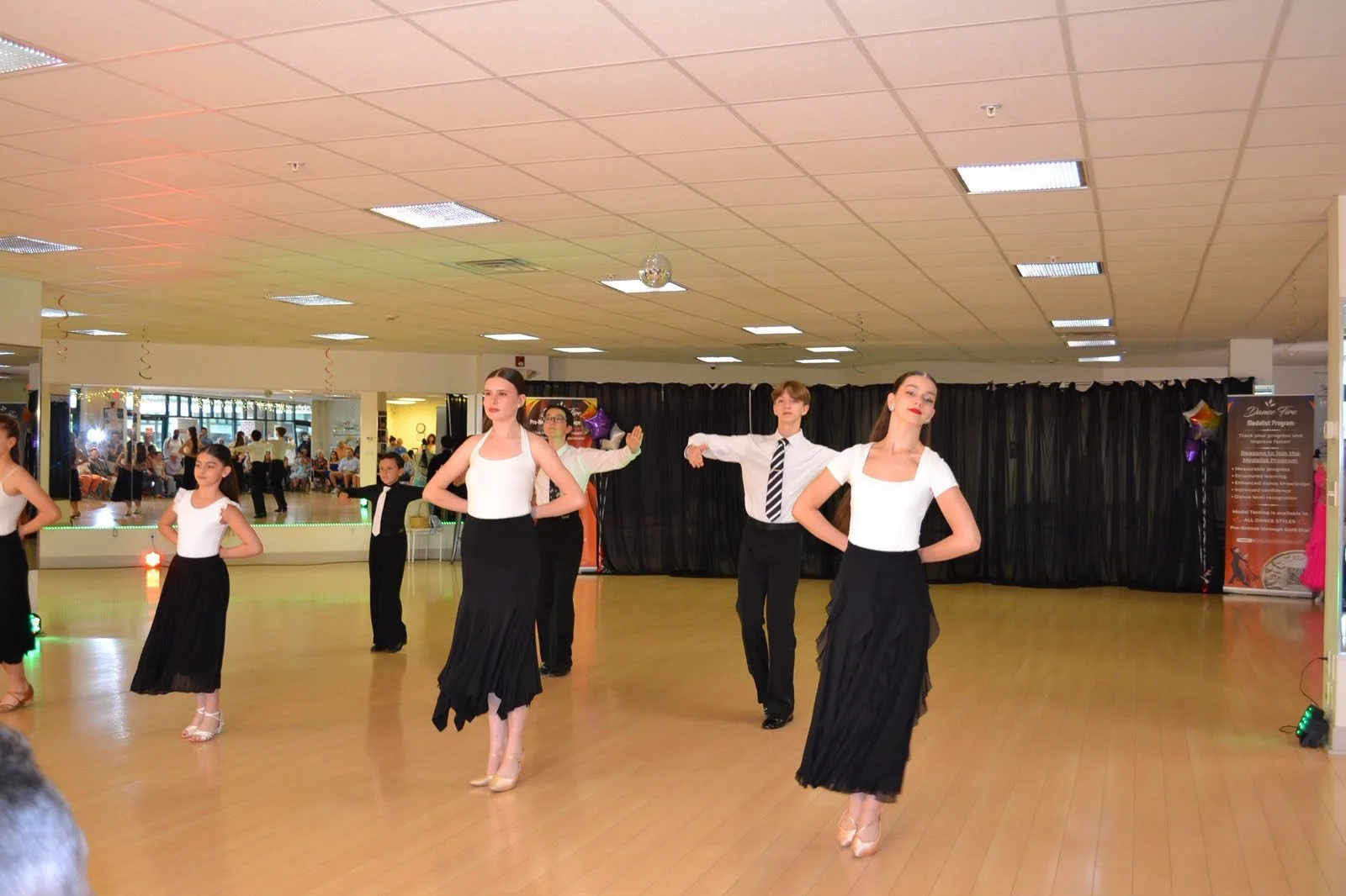Young dancers in white tops and black skirts perform a group routine