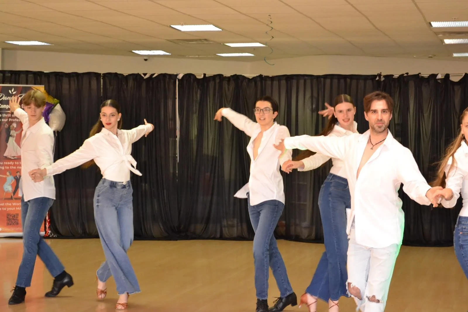 Youth performers in white shirts and jeans extend their arms together