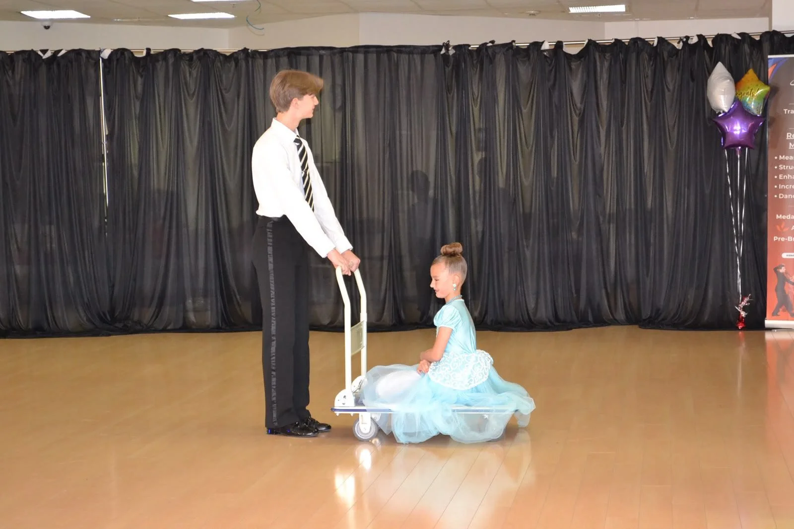 A ballroom pair holds a theatrical pose with one dancer seated on the floor