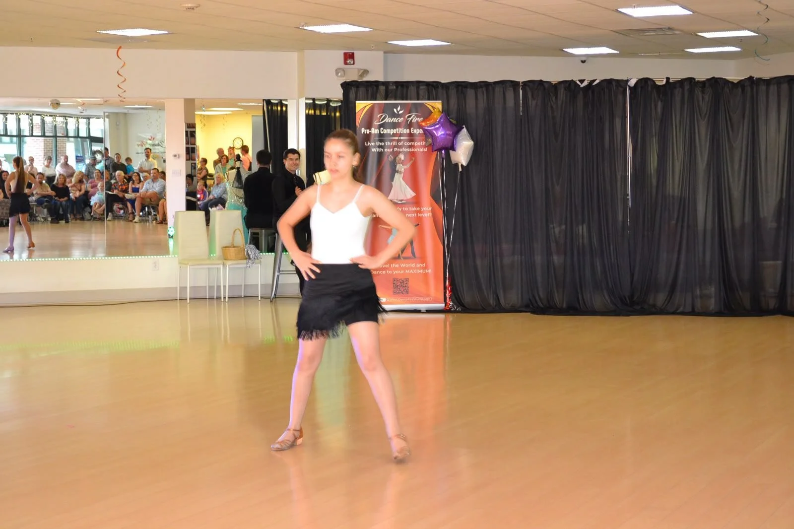 A young performer holds a recital pose in a white top and black skirt