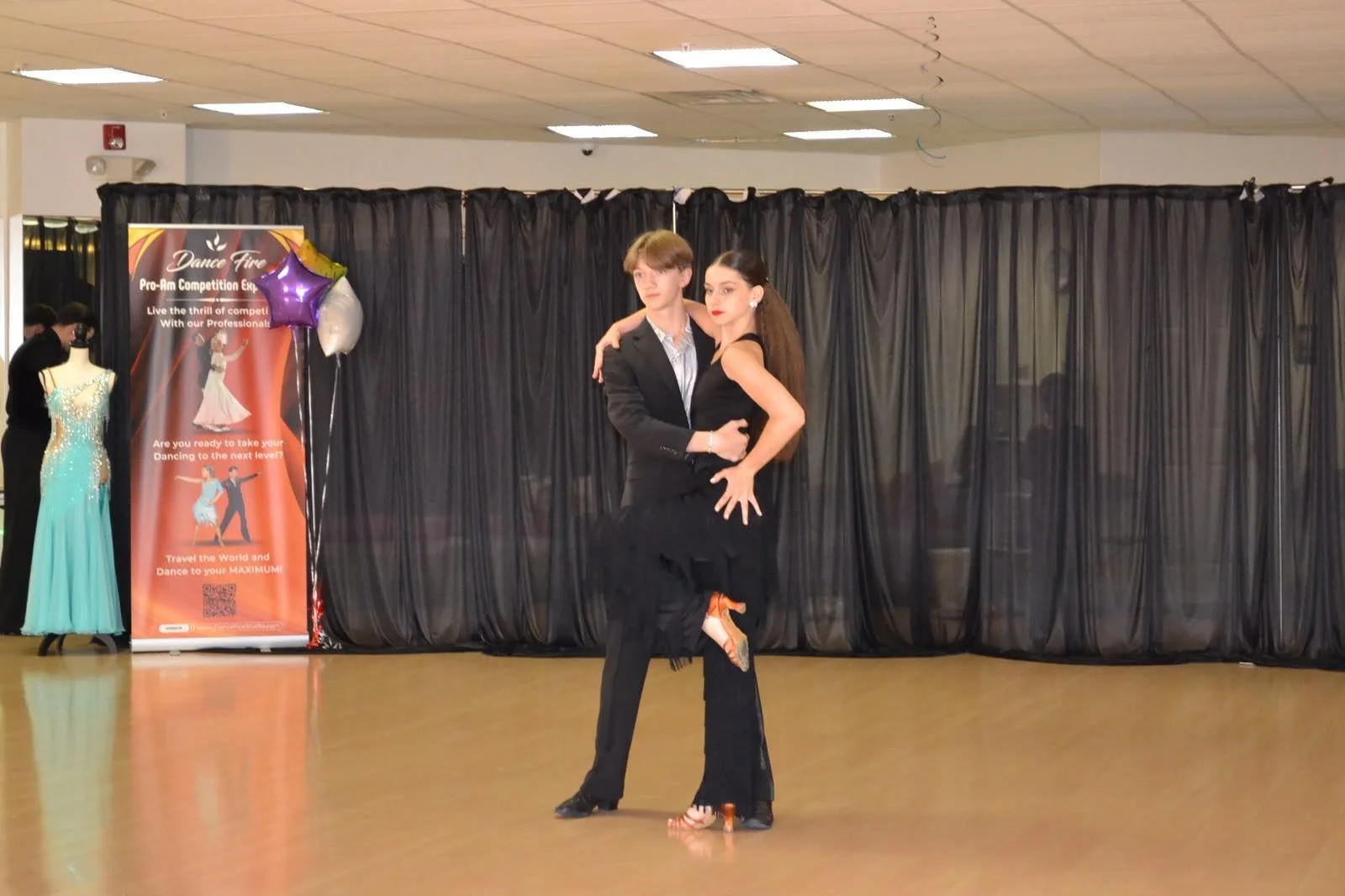 A young dance pair in black performs together before the studio curtains