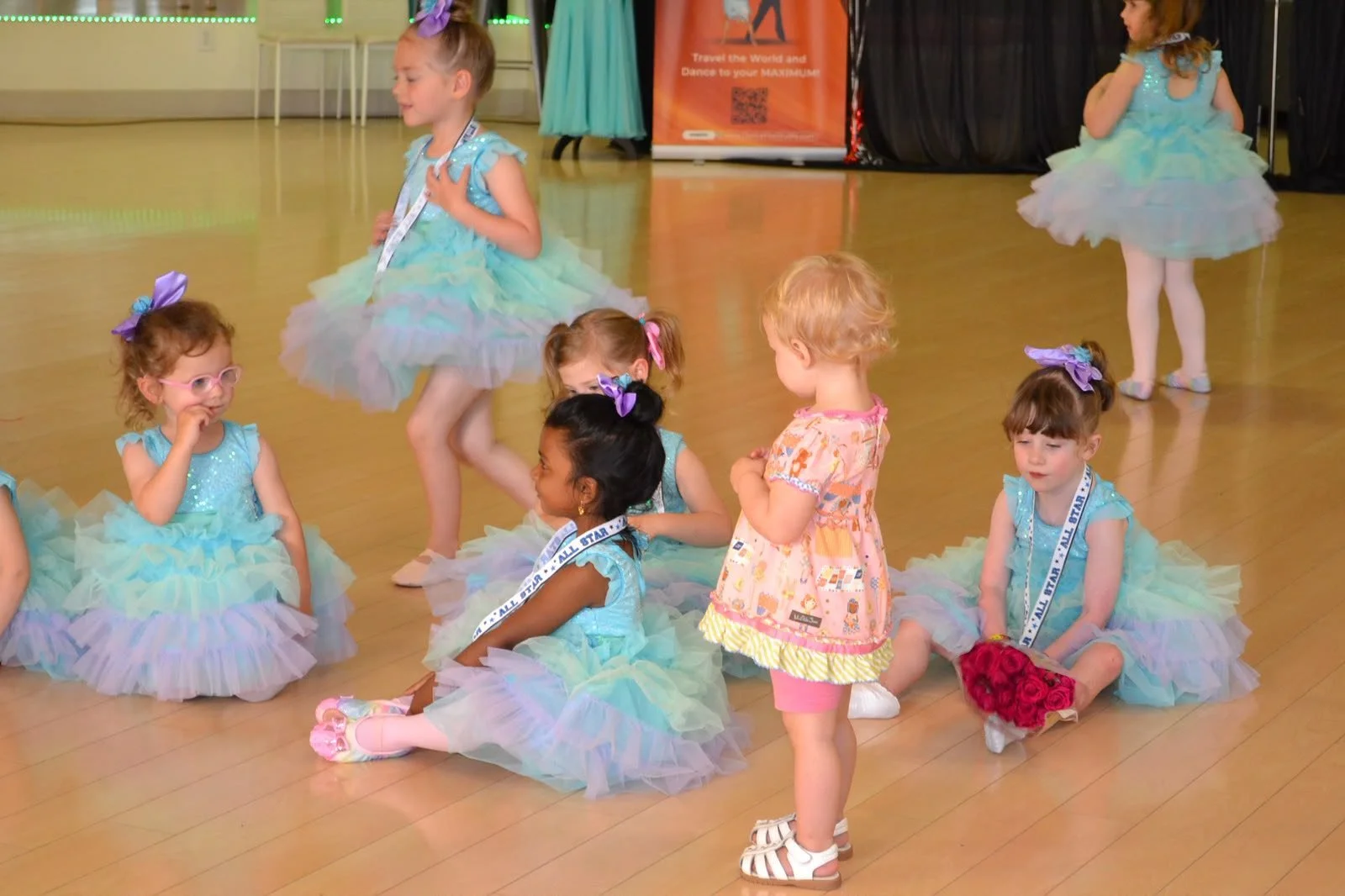 Young ballet performers sit together in pastel tutus during their routine