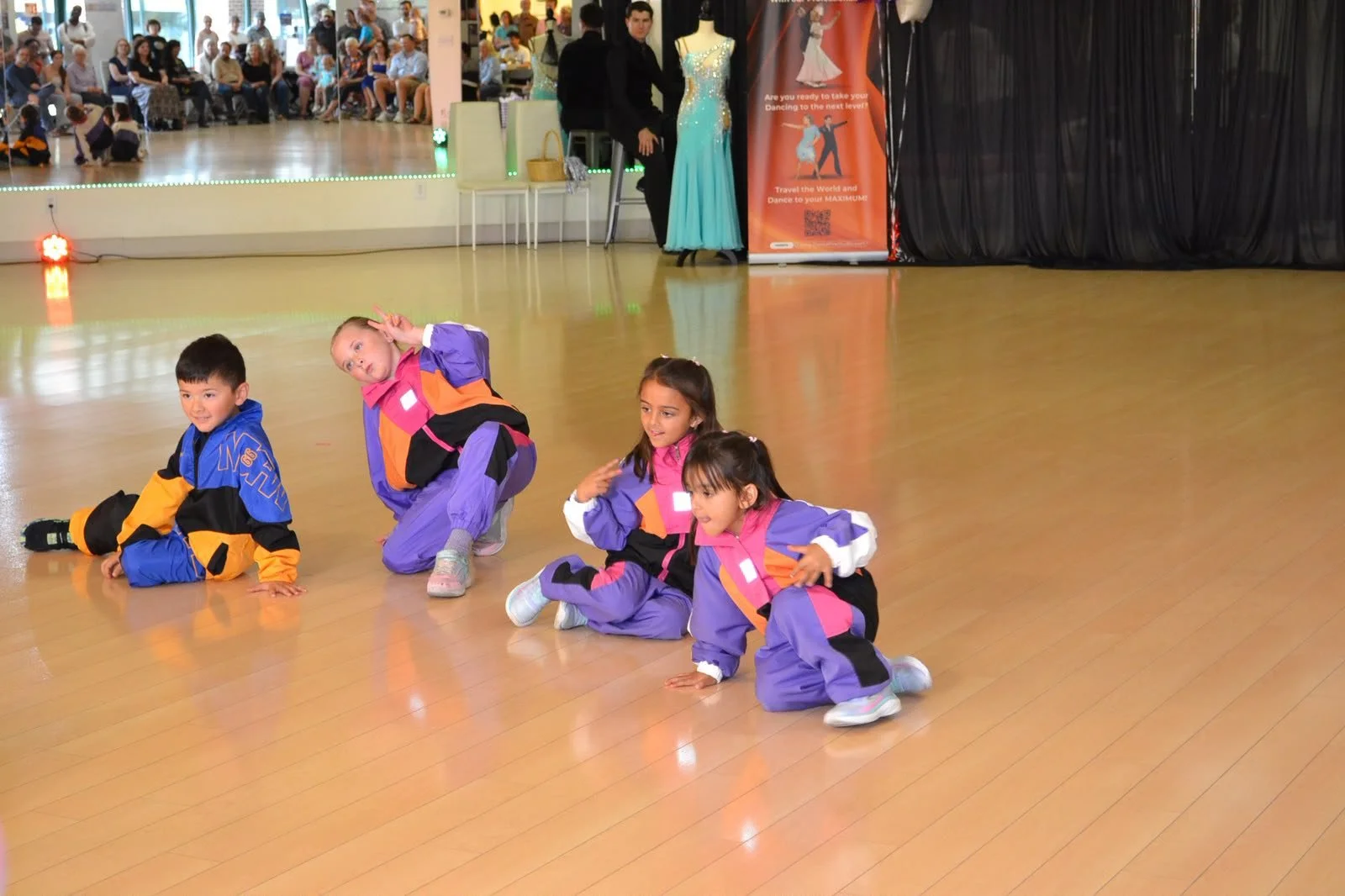 Children in purple recital costumes perform a seated group movement