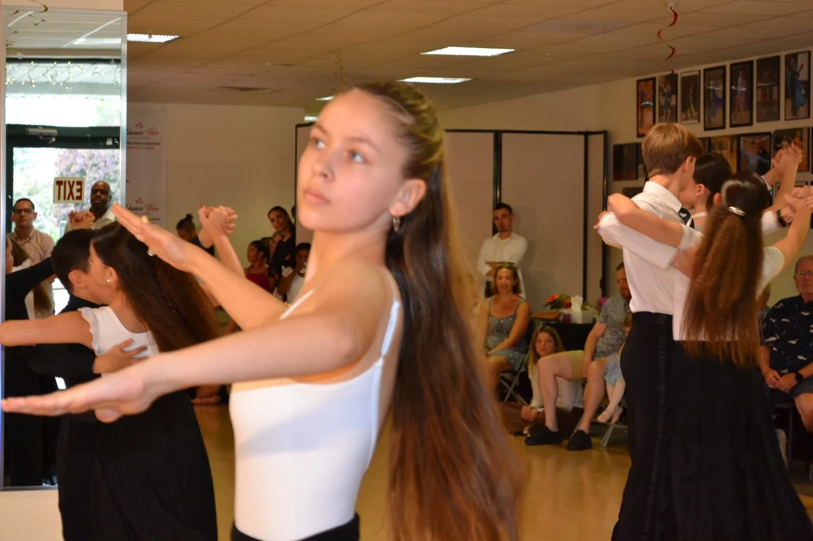 A young dancer in a white top performs near the recital audience