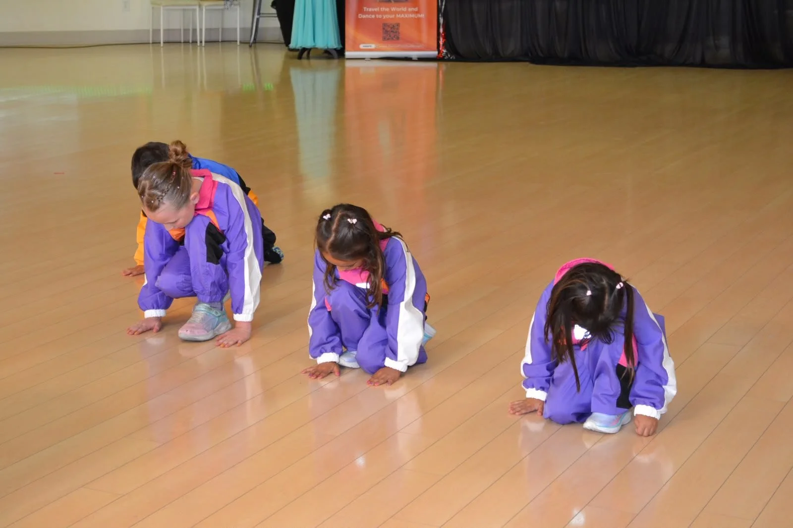 Young performers in purple costumes kneel together during a floor sequence