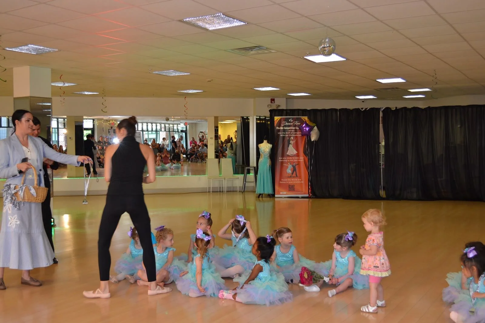 An instructor guides young ballet performers seated in pastel tutus