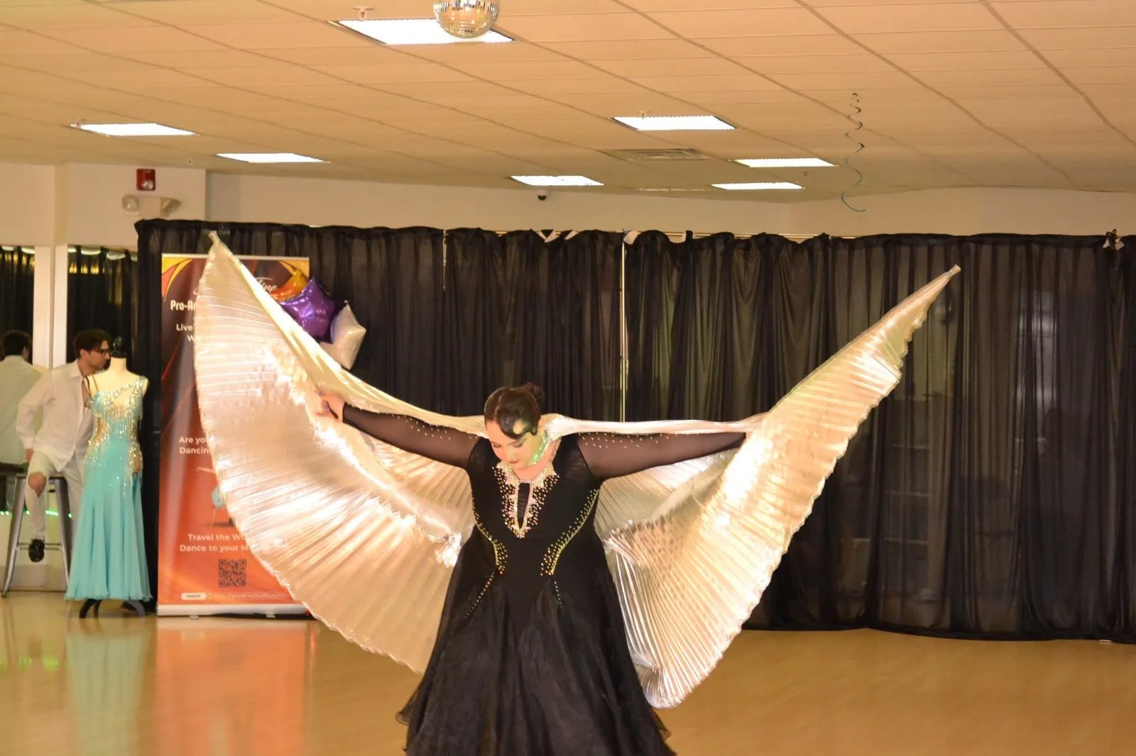 A recital performer extends butterfly-style wings before the studio backdrop