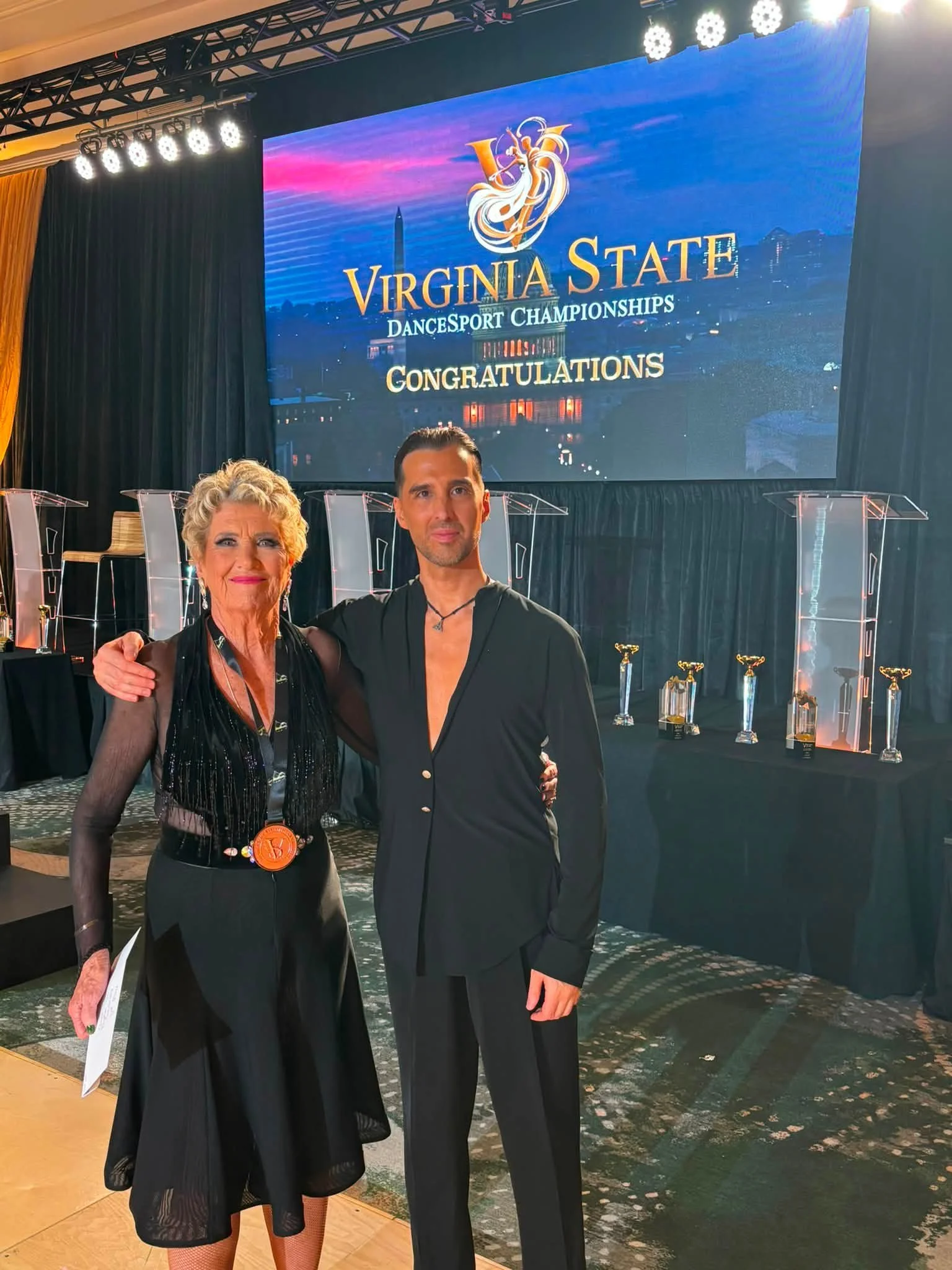 A Dance Fire competition pair poses beside the Virginia event display