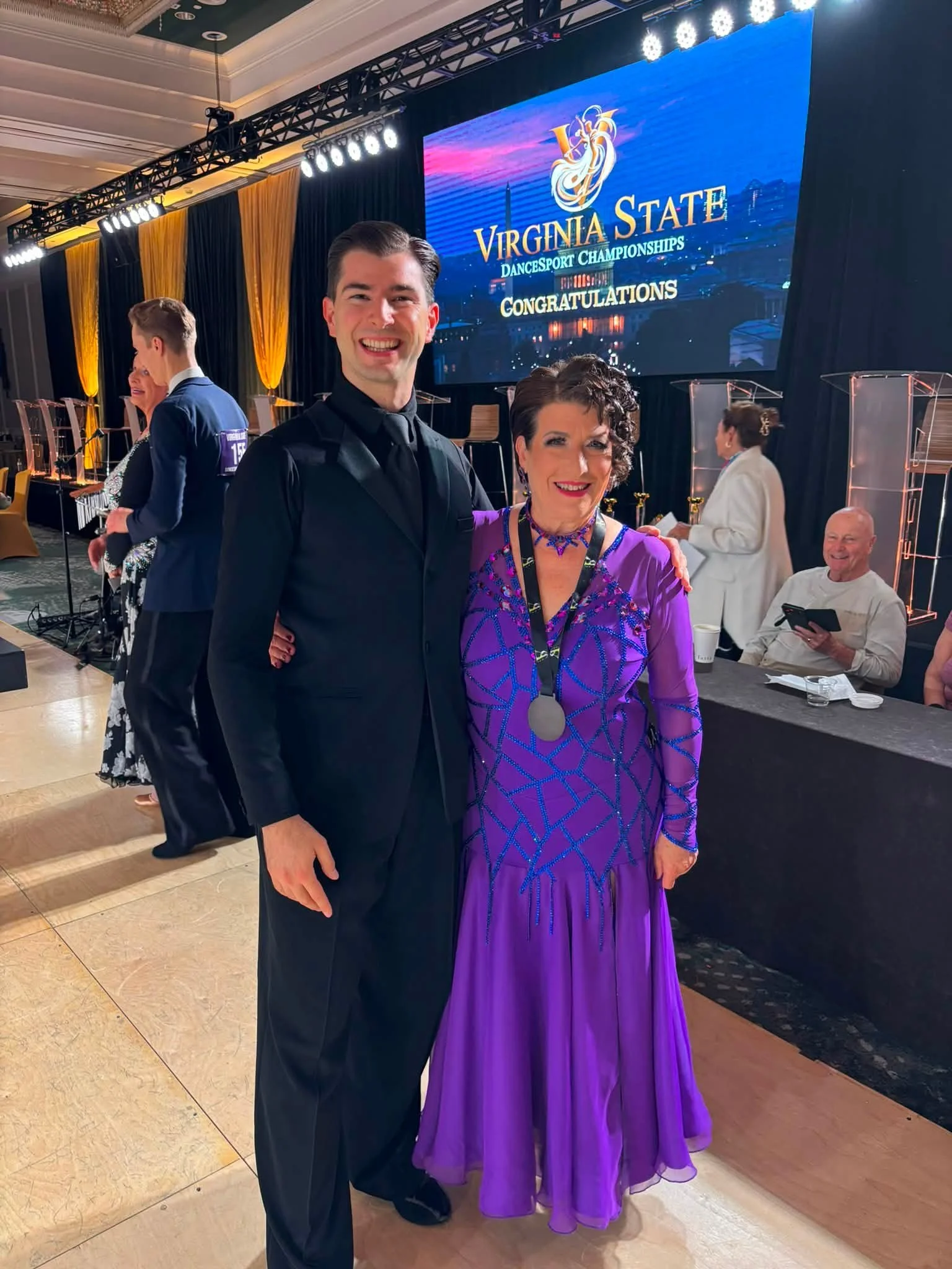 A Dance Fire ballroom pair poses in purple and black competition attire