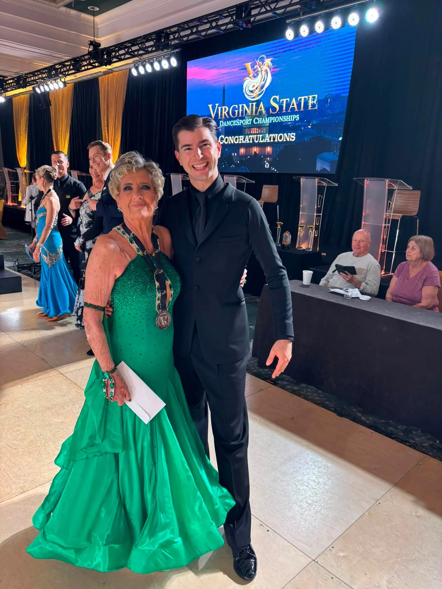 A Dance Fire ballroom pair poses in green and black competition attire