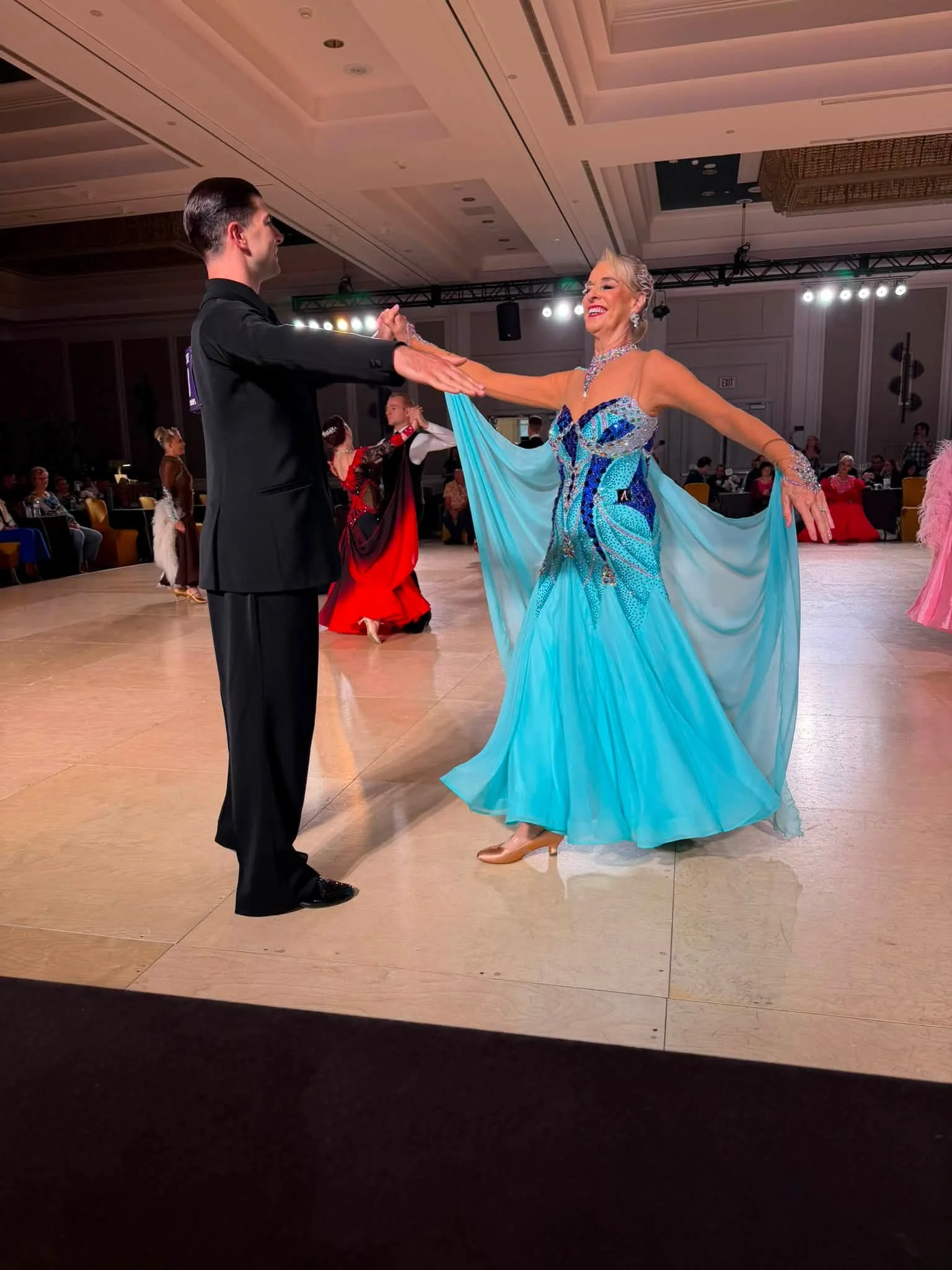 A couple in turquoise and black dances across the Virginia ballroom floor