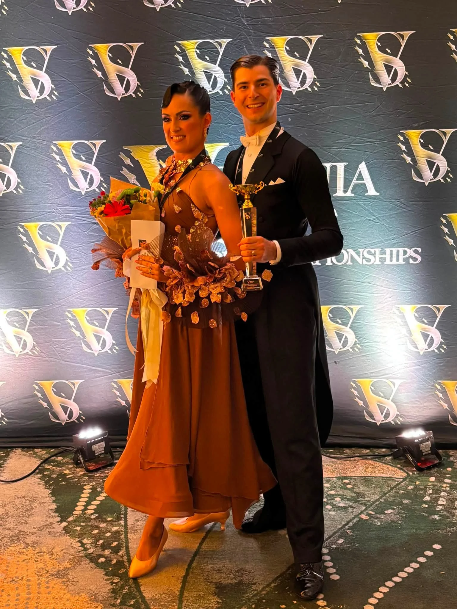 A professional ballroom pair poses with flowers at the Virginia event backdrop