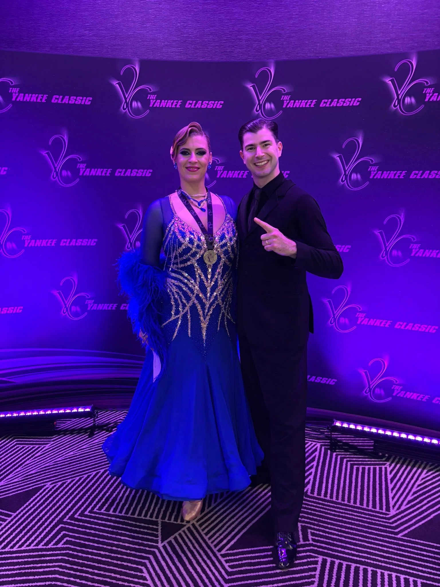 A ballroom couple poses at the Yankee Classic competition backdrop