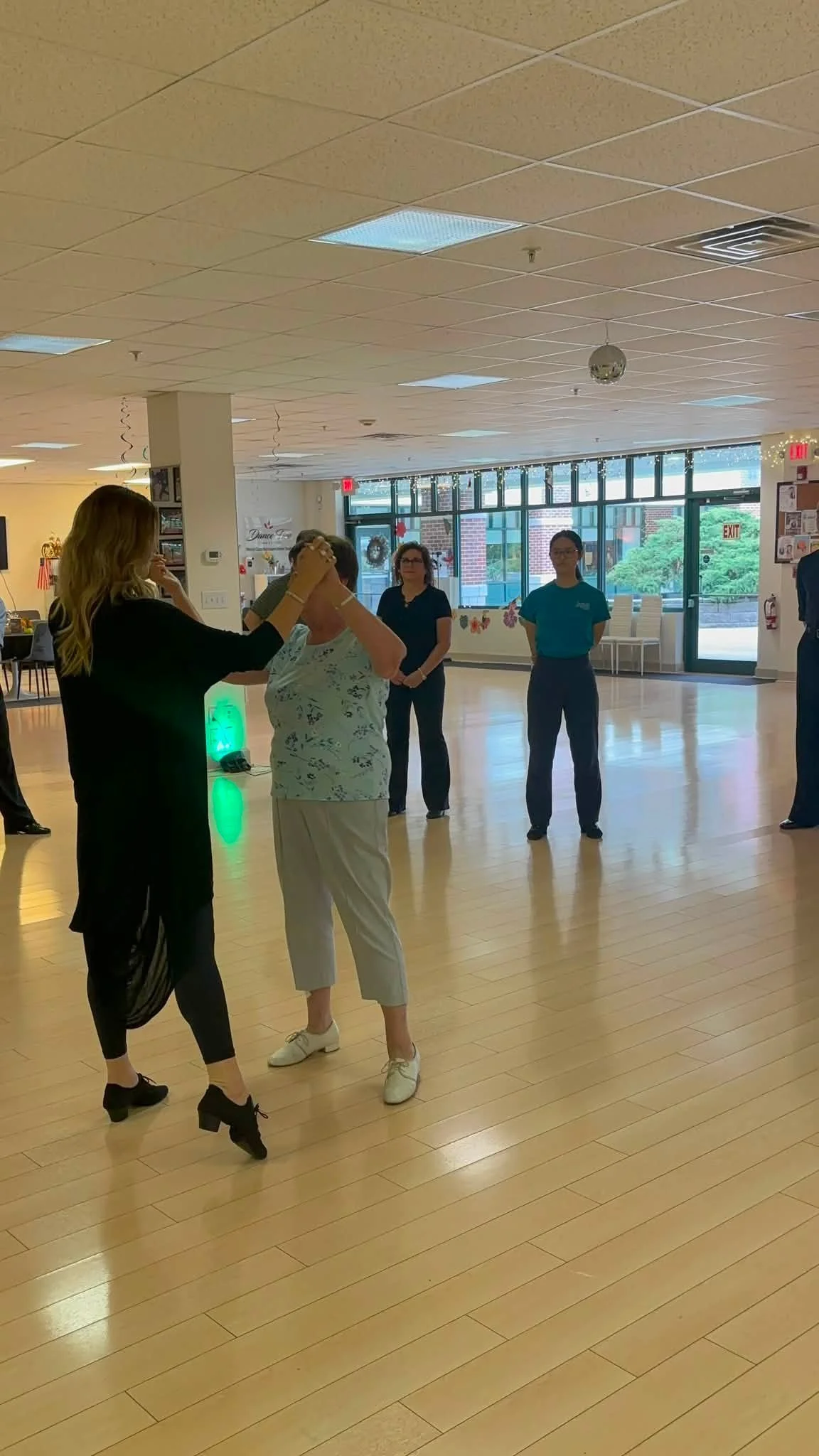 A coaching pair practices while classmates observe near the studio mirrors