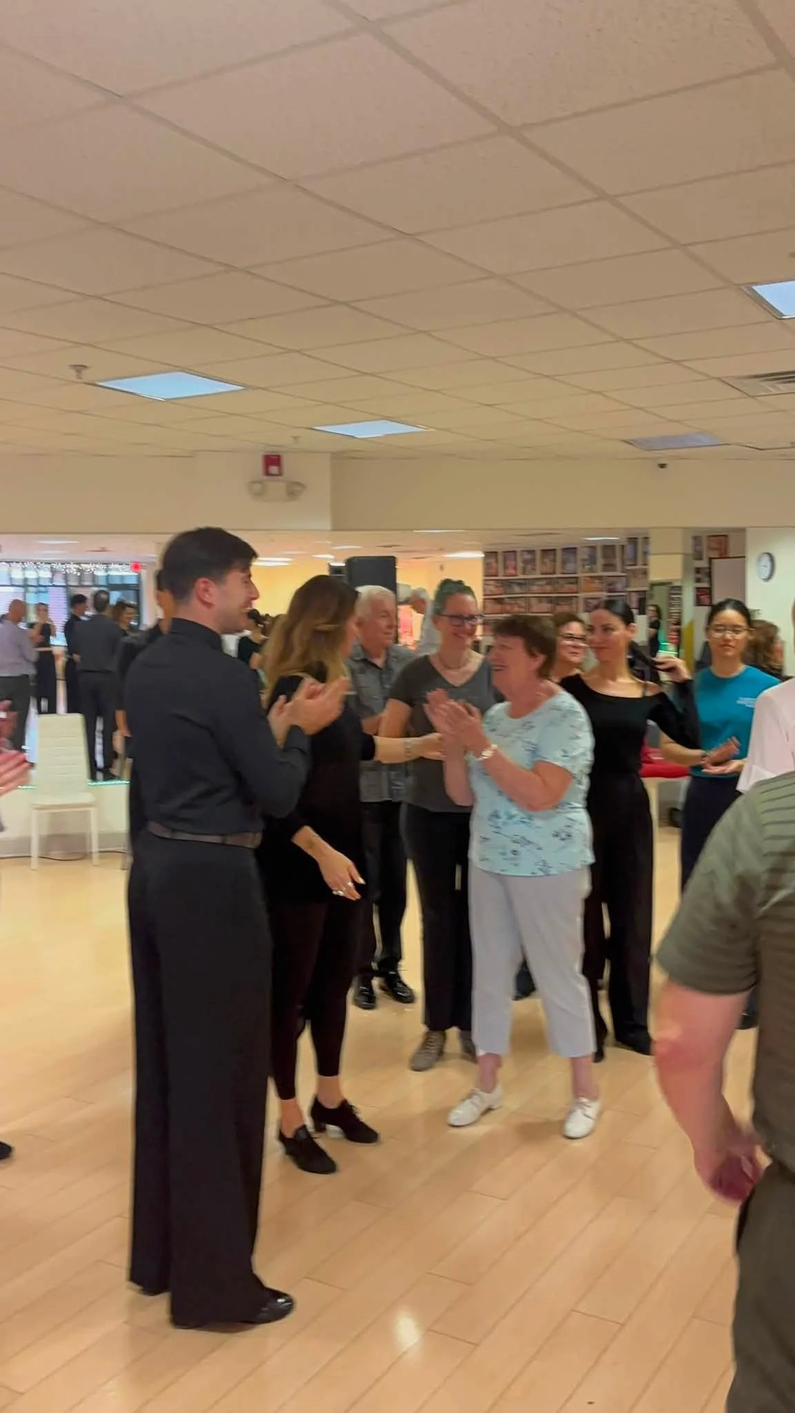 The class gathers around an instructor demonstrating partnered dance technique