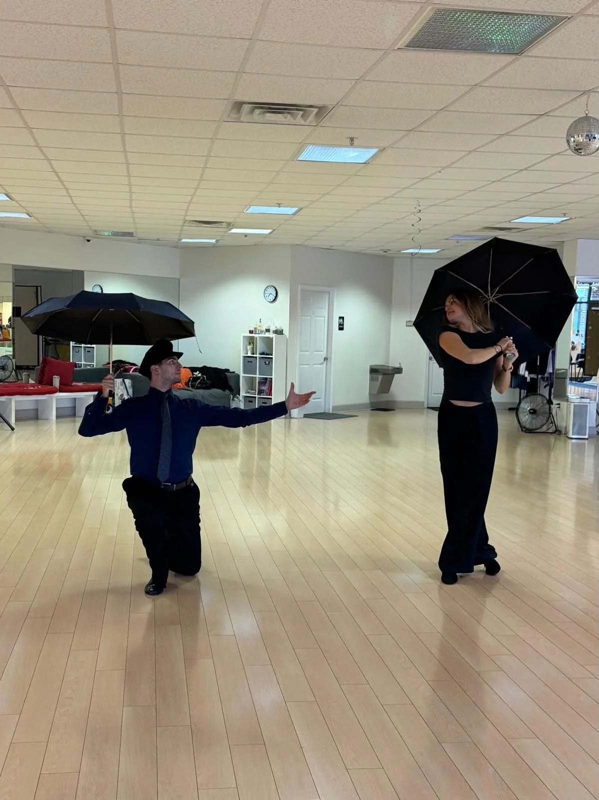 Two coaching participants practice with open umbrellas on the studio floor