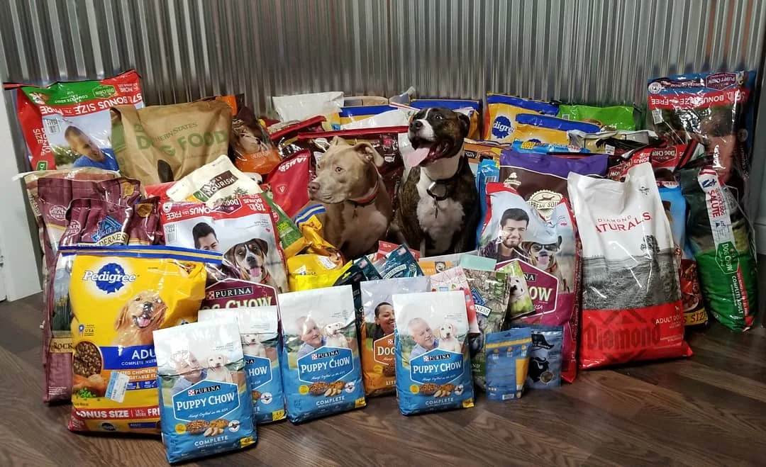 This is a photo of the 856lbs of dog food we collected at this year’s event with our two Pitbulls, Caesar (dark brindle) & Alpha (light brown). They are so glad we all help their doggie friends have full bellies!