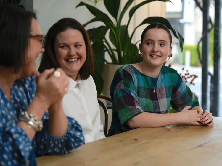 Three women sitting around a wooden table smiling during a social media strategy session.