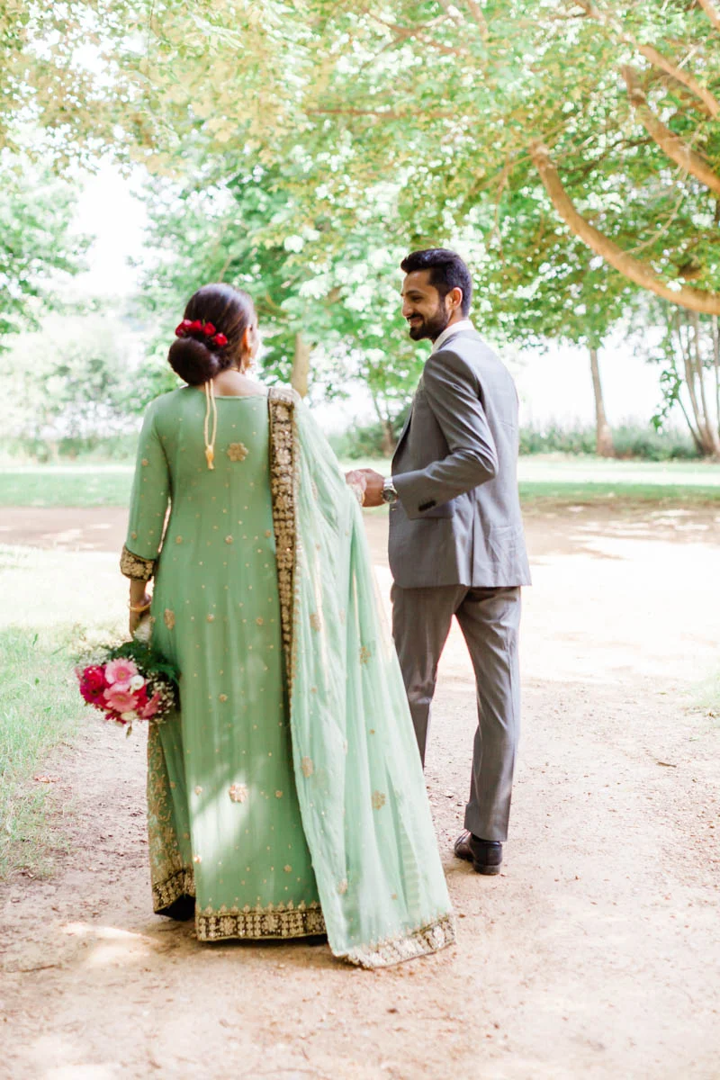 Indian woman wearing long green and gold dress holding bouquet of pink flowers at her engagement session