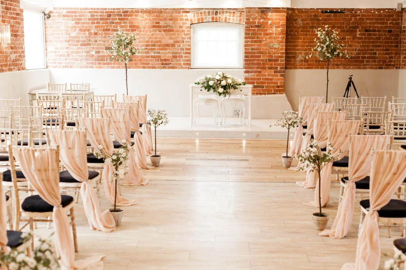 ceremony room decorated with pale pink chair covers at Sopley Mill in Dorsetbride and groom kiss eachother at the alter of the cerony
