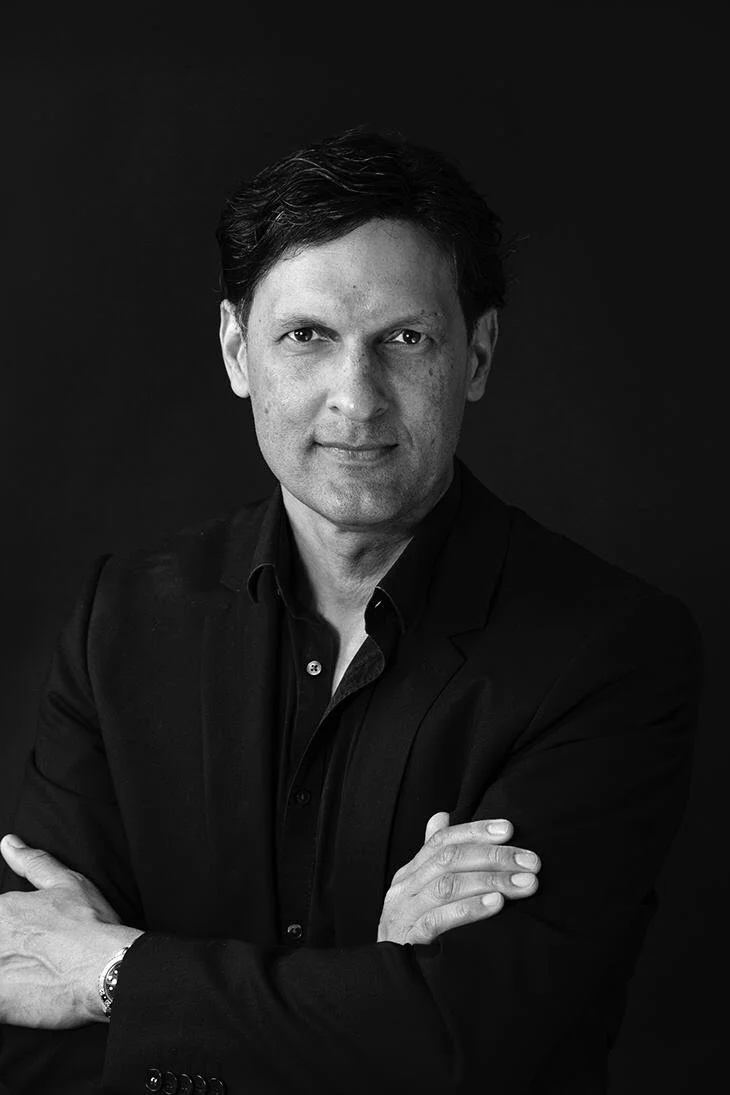 Zwart-wit portret van een man in een pak met gekruiste armen, neutrale achtergrond.
