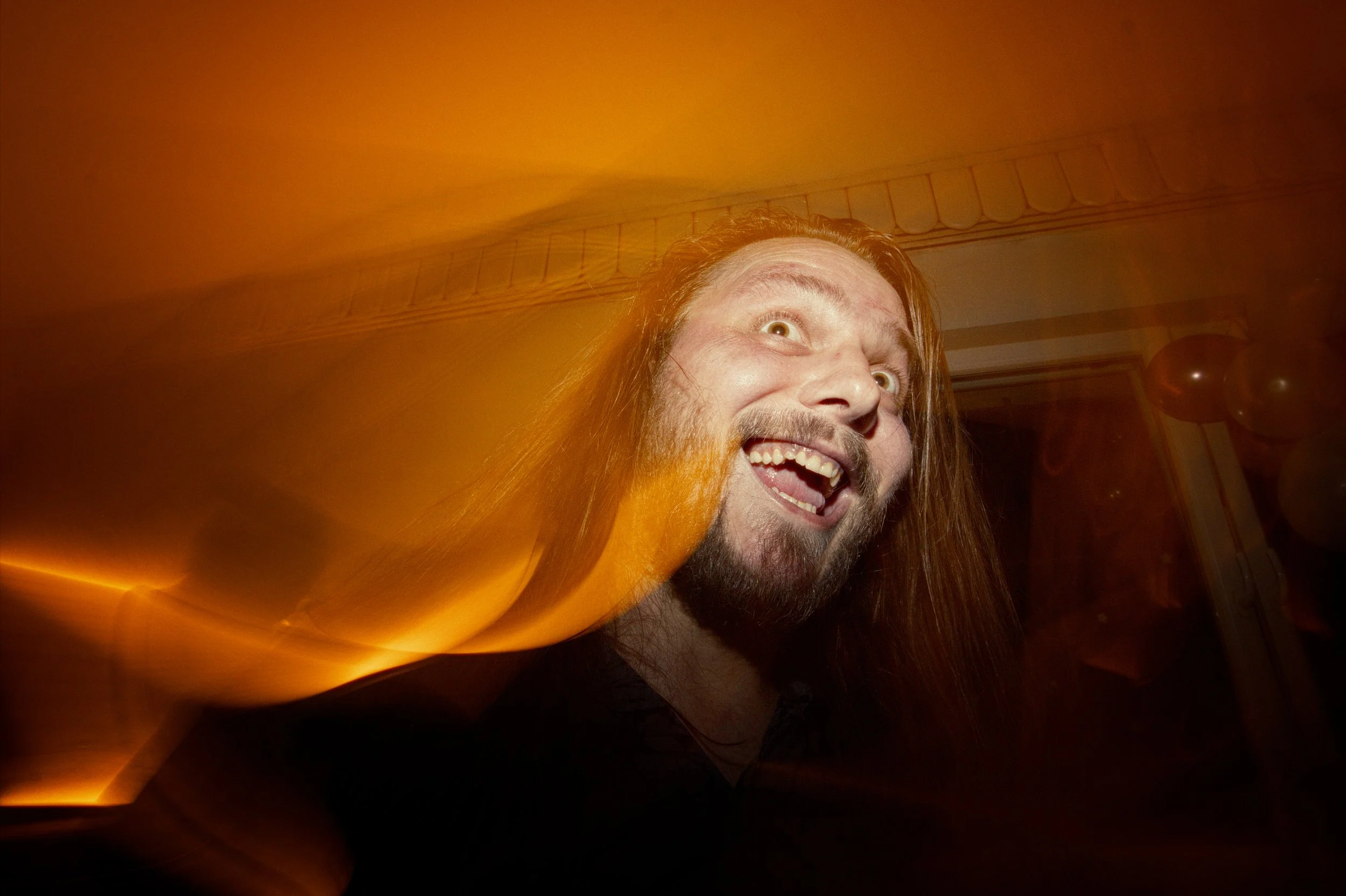 A man with long hair and a beard smiling and making a funny face, shot with a motion blur effect.