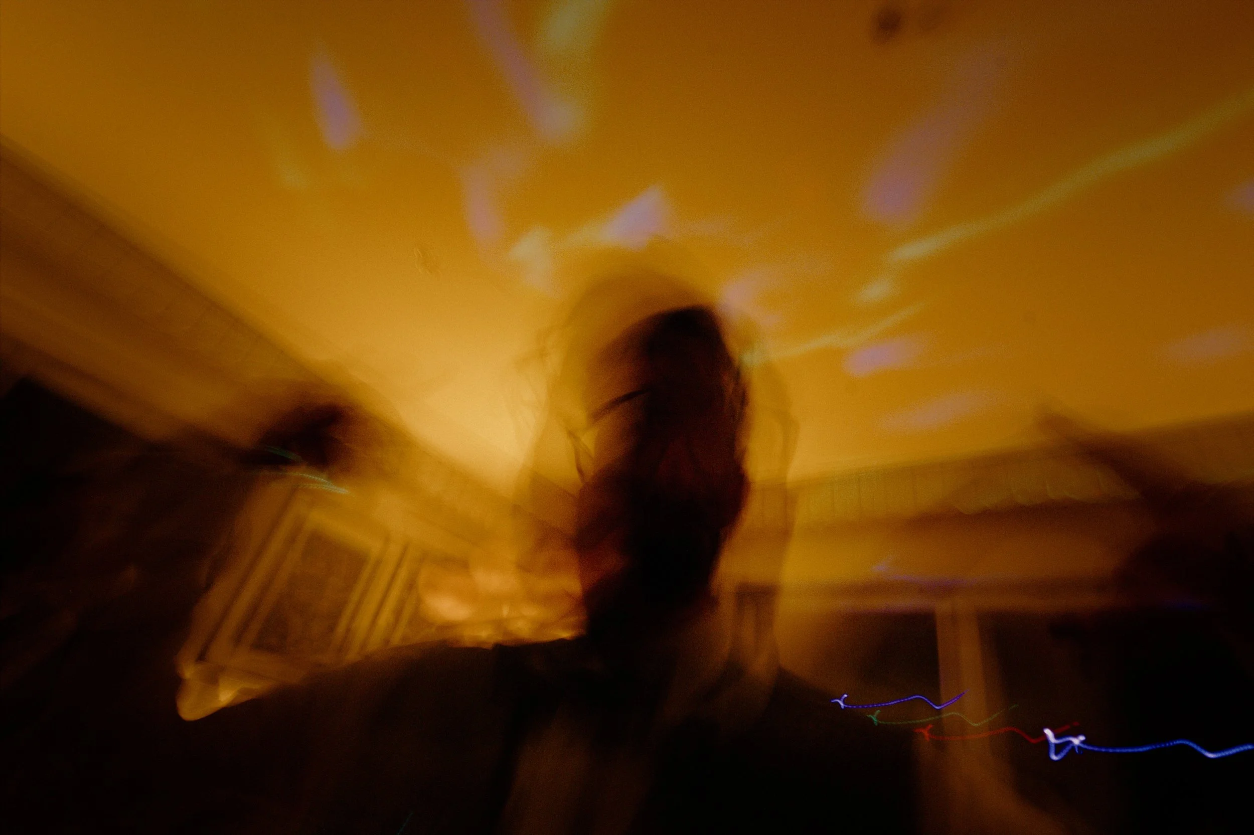 Blurry photo of a person in a dimly lit room with yellowish lighting and colorful light streaks.