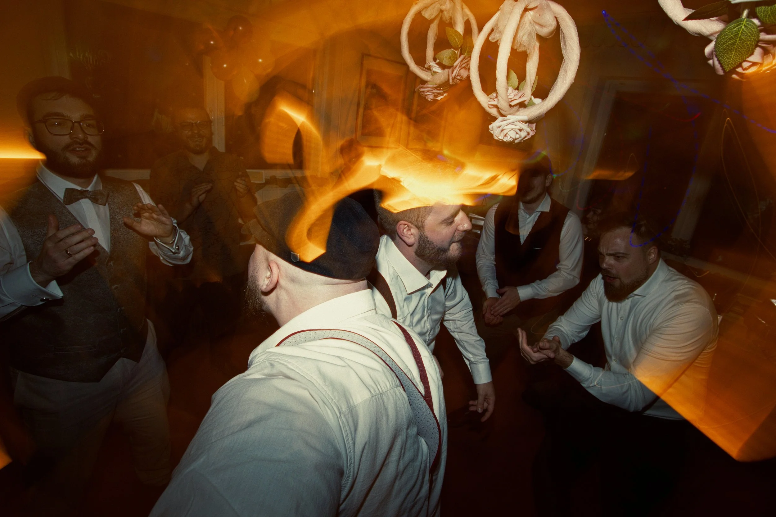 Group of men dancing and socializing at a celebration or party with colorful decorations and dramatic lighting.