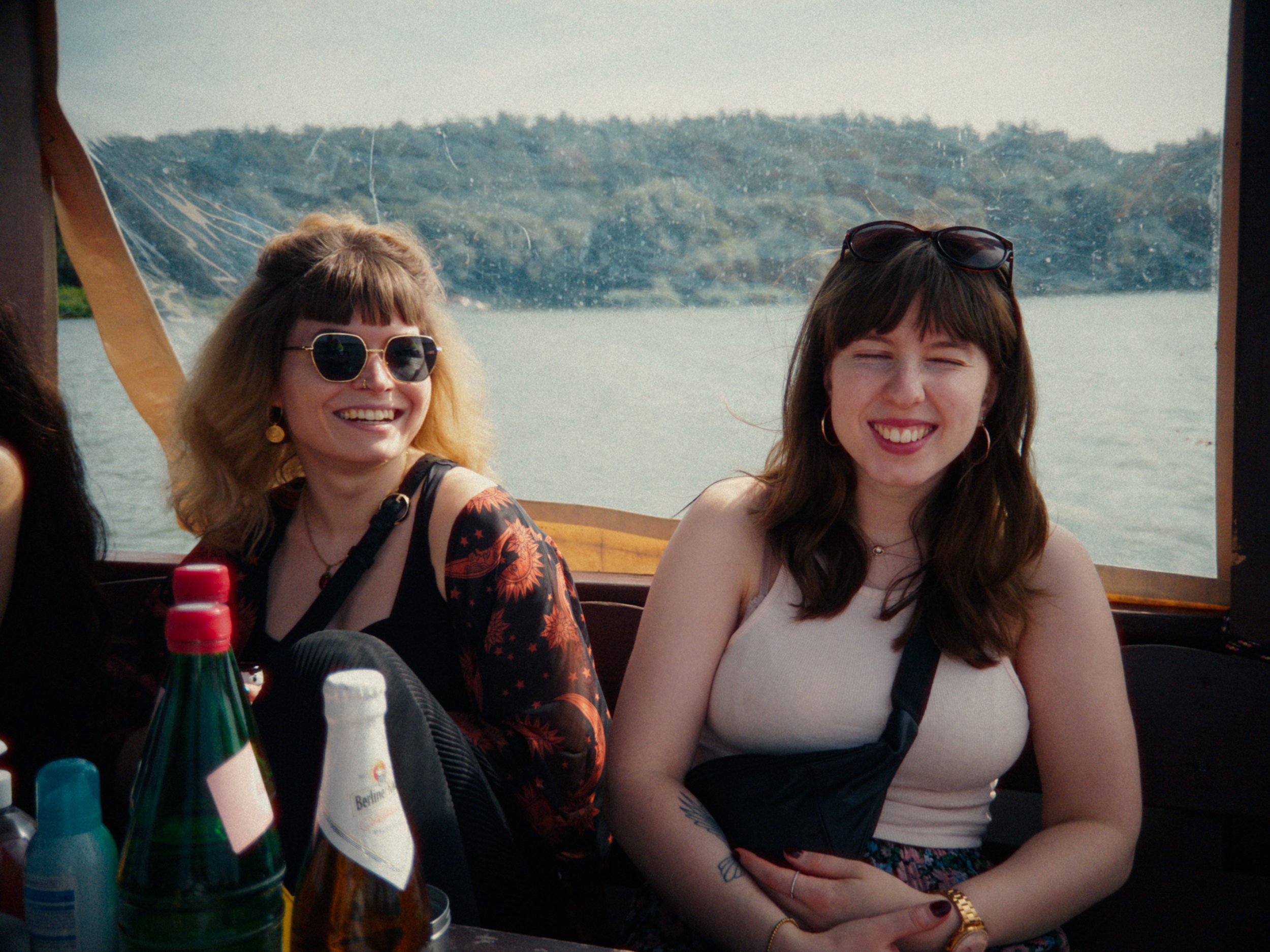 Two women smiling and enjoying a boat ride on a body of water with trees in the background.