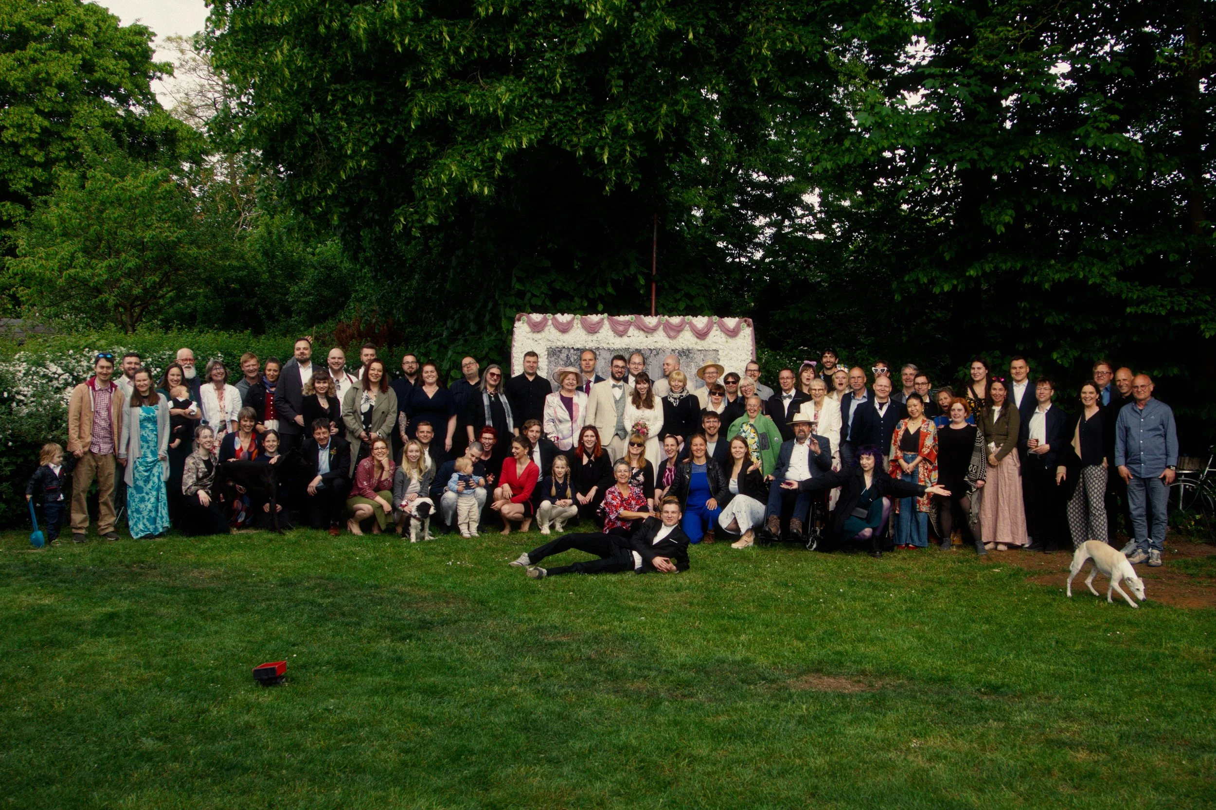 A large group of people gathered outdoors on a green lawn, with trees in the background, for a group photo at a celebration or event.