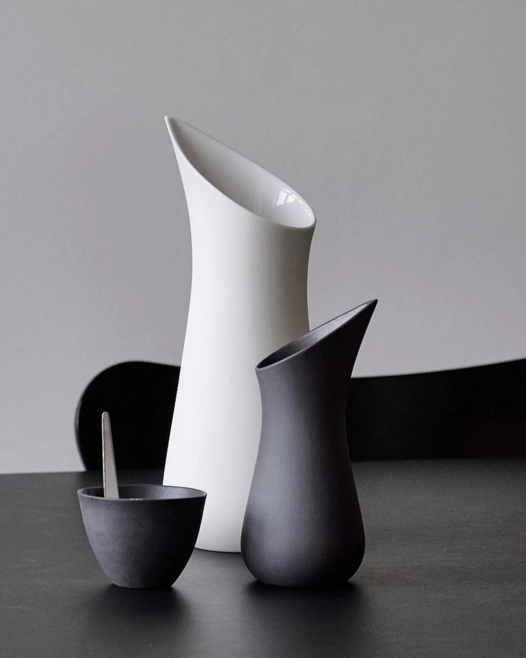 White and black handmade porcelain jugs with a matching black bowl on a table, showcasing timeless Scandinavian design.