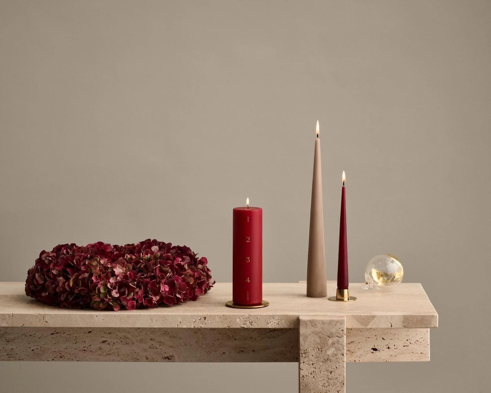 Ester & Erik red Advent candle numbered 1–4 with two lit taper candles and red hydrangeas on a stone table.