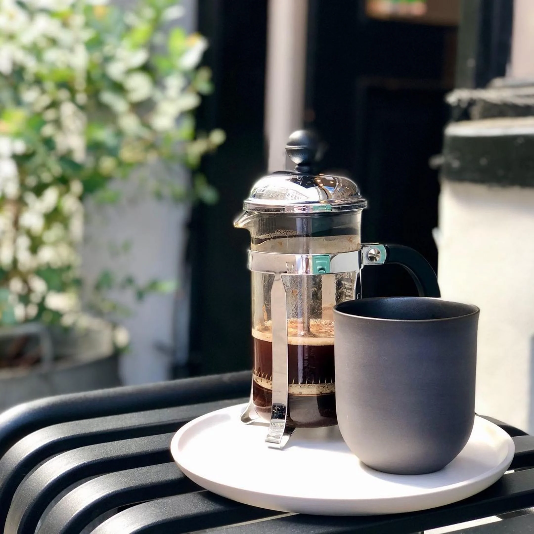 Handcrafted Danish ceramic mug and French coffee press on sunny bench