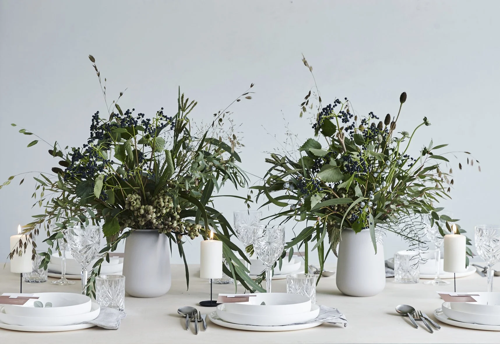 lassic Scandinavian vases with winter greens arranged on a set table