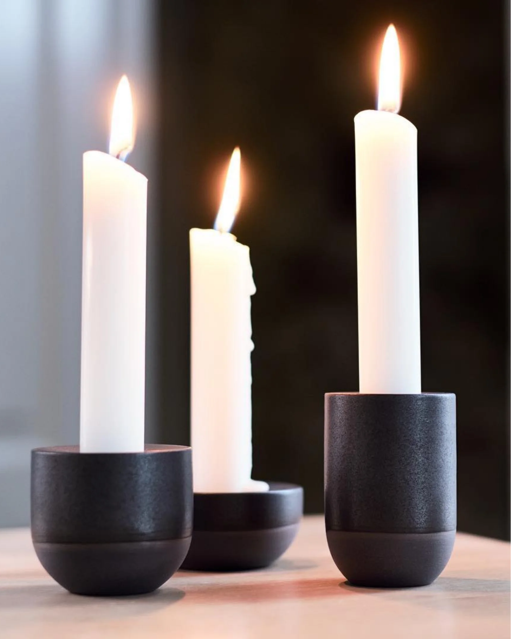 Three handmade black porcelain candle holders with lit white taper candles, bringing warm Scandinavian style to the table.